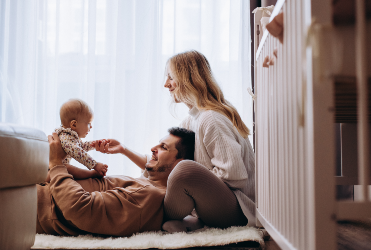 father laying on the floor holding baby with wife next to him